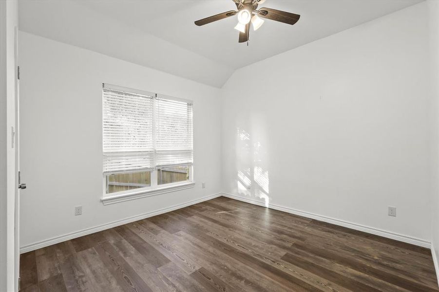 Empty room with ceiling fan, vaulted ceiling, and dark hardwood / wood-style floors