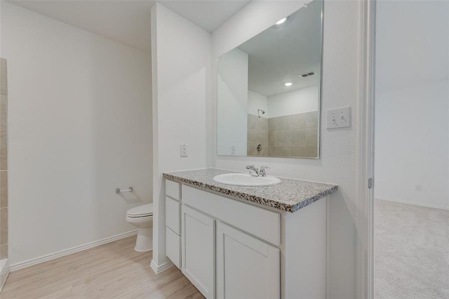 Bathroom with hardwood / wood-style floors, a tile shower, vanity, and toilet