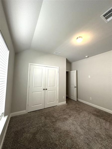 Unfurnished bedroom with lofted ceiling, a textured ceiling, a closet, and carpet