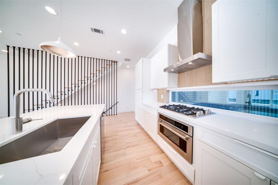 Kitchen with wall chimney range hood, white cabinets, light hardwood / wood-style flooring, stainless steel appliances, and decorative light fixtures