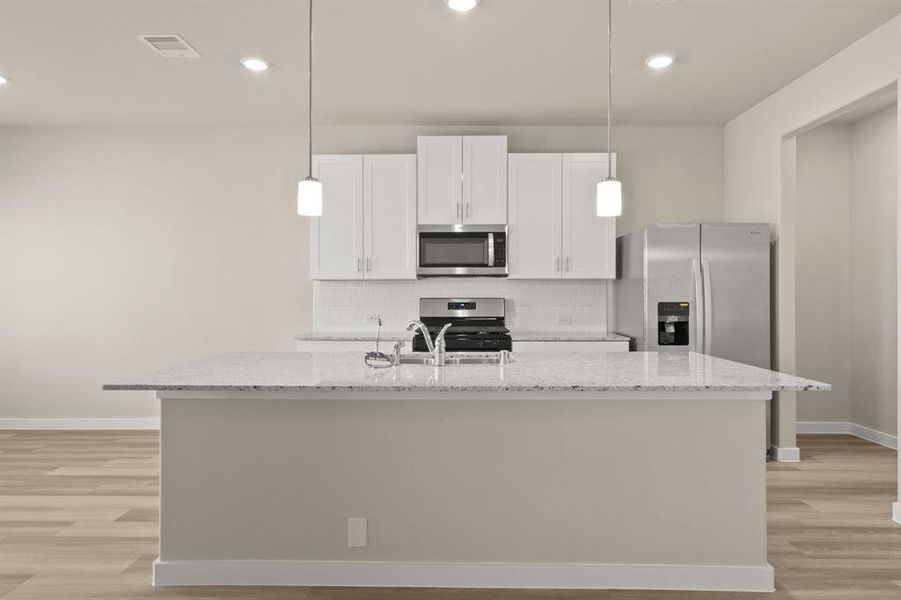 An additional view of the Gourmet Kitchen with pendant lighting, custom backsplash, and oversized kitchen island w/ breakfast bar.