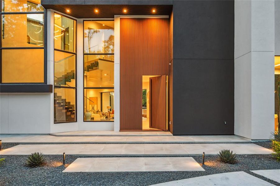 A stunning front entrance is highlighted by elegant architectural details and tasteful landscaping. The inviting entryway sets the tone for the home's refined aesthetic and welcoming atmosphere. A custom pivoting steel front door imported from Austin adds a unique and sophisticated touch to the entryway. This distinctive door combines modern design with exceptional craftsmanship, making a bold statement and enhancing the home's curb appeal.