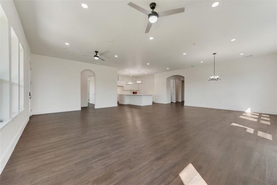 Unfurnished living room with ceiling fan with notable chandelier and dark hardwood / wood-style flooring