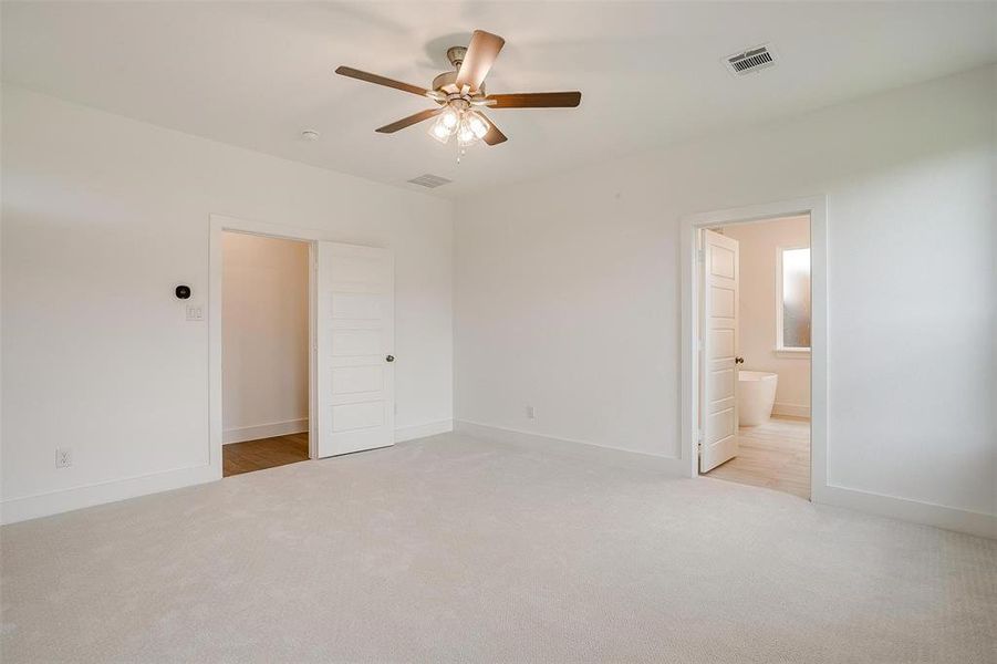 Unfurnished bedroom featuring light carpet, ensuite bathroom, and ceiling fan