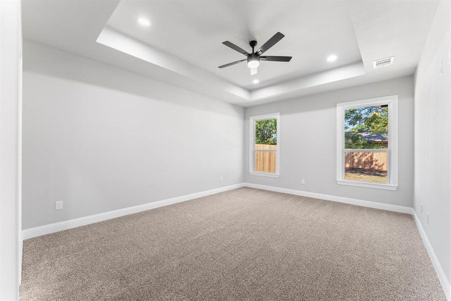 Empty room with carpet, a tray ceiling, and ceiling fan