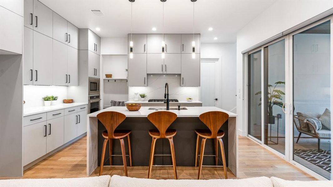 Kitchen with decorative light fixtures, light hardwood / wood-style flooring, a center island with sink, appliances with stainless steel finishes, and a breakfast bar