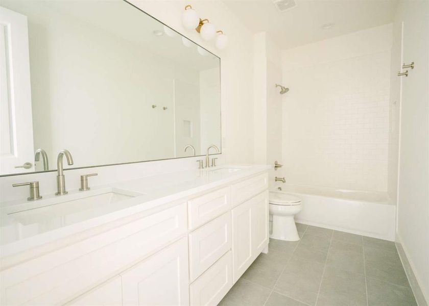 Full bathroom featuring double vanity, tile flooring, toilet, and tiled shower / bath