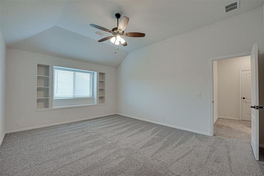 Spare room featuring vaulted ceiling, built in features, carpet floors, and ceiling fan