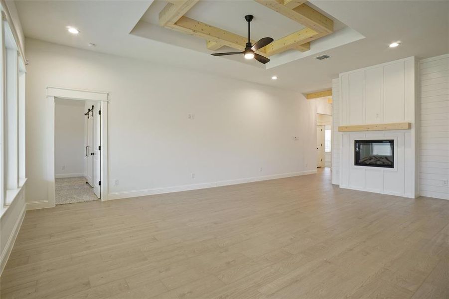 Unfurnished living room with a fireplace, ceiling fan, a raised ceiling, and light hardwood / wood-style floors