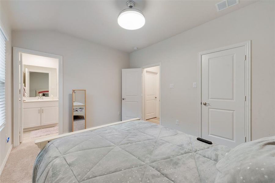 Bedroom with ensuite bath, vaulted ceiling, and light colored carpet