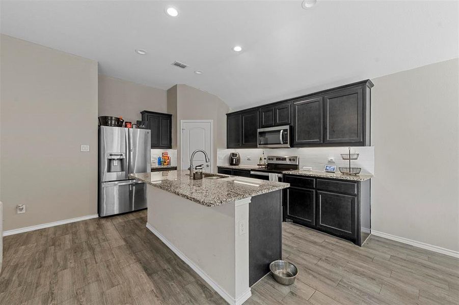 Kitchen with light stone countertops, sink, light wood-type flooring, an island with sink, and stainless steel appliances