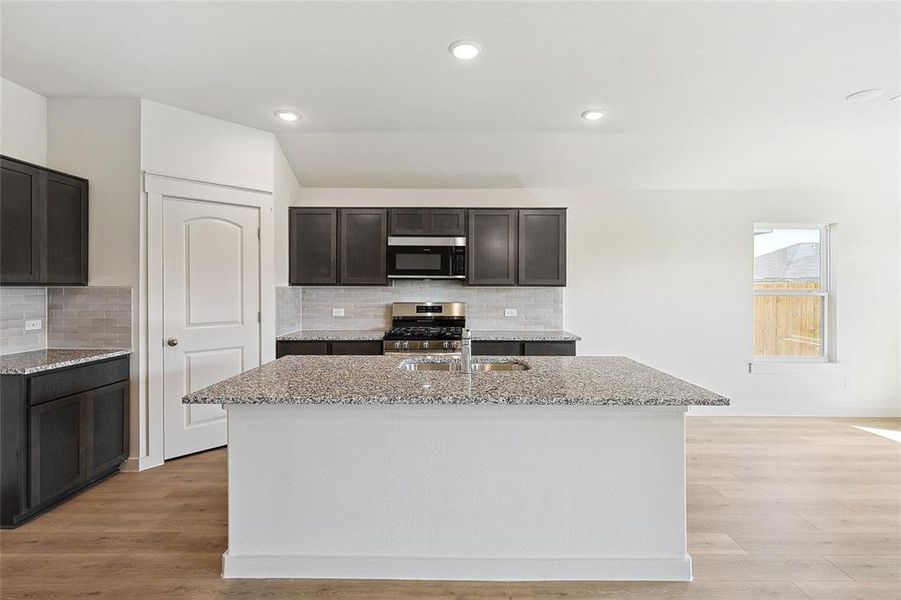 Kitchen with light stone countertops, an island with sink, stainless steel appliances, and light hardwood / wood-style flooring