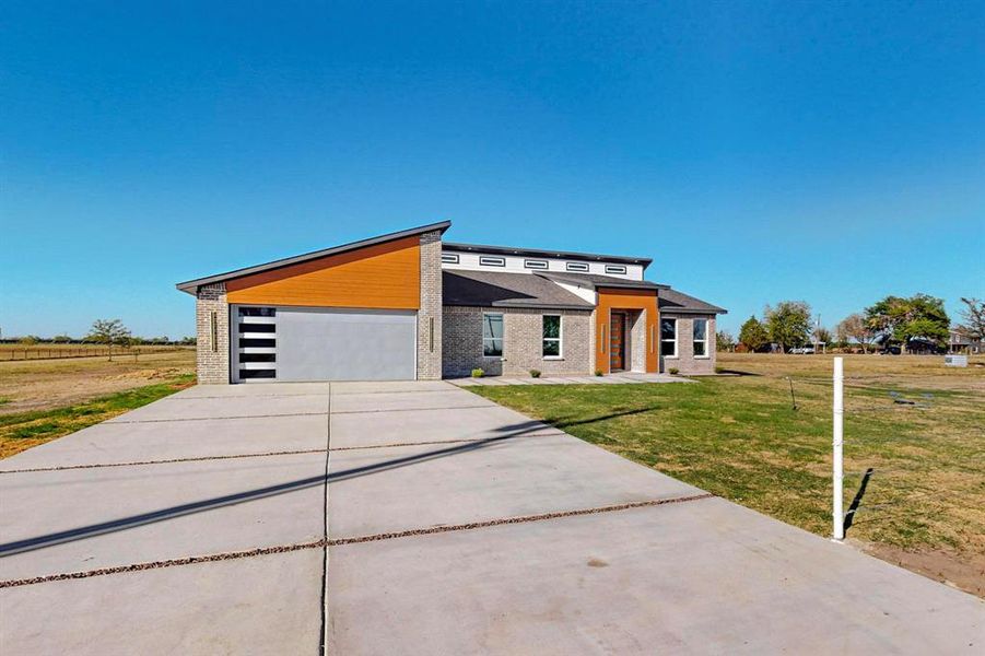 View of front facade featuring a front yard, a garage, and a rural view