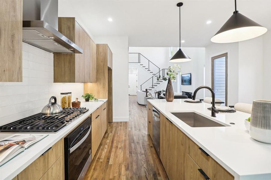 Kitchen with dark hardwood / wood-style floors, stainless steel appliances, sink, wall chimney exhaust hood, and decorative light fixtures