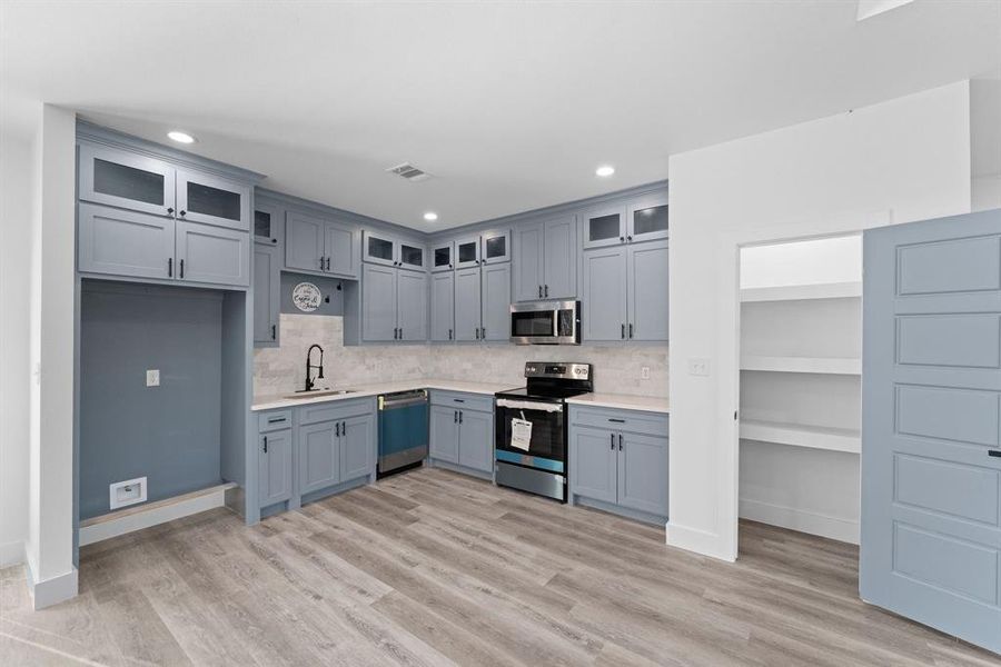 Kitchen featuring light wood-type flooring, backsplash, sink, and stainless steel appliances