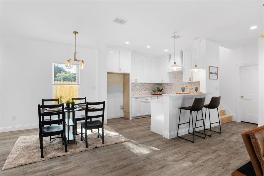 Kitchen with a kitchen breakfast bar, light hardwood / wood-style flooring, a notable chandelier, hanging light fixtures, and white cabinetry