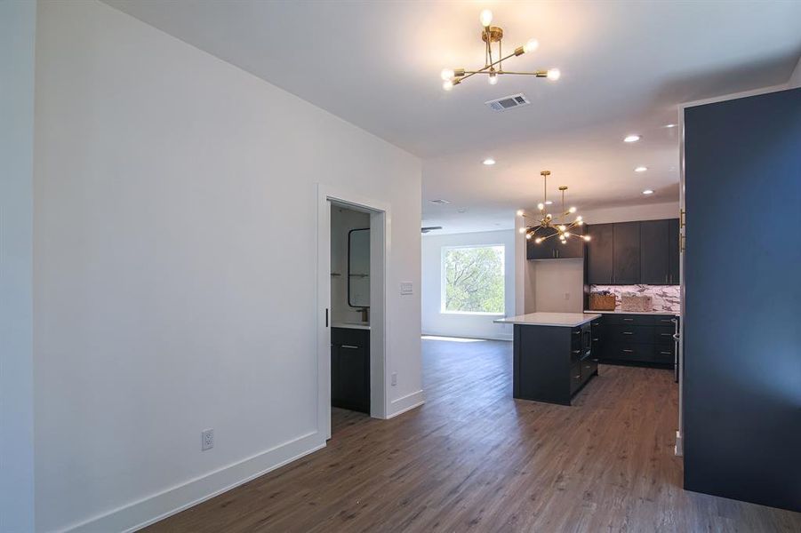 Kitchen with pendant lighting, tasteful backsplash, a kitchen island, dark wood-type flooring, and an inviting chandelier