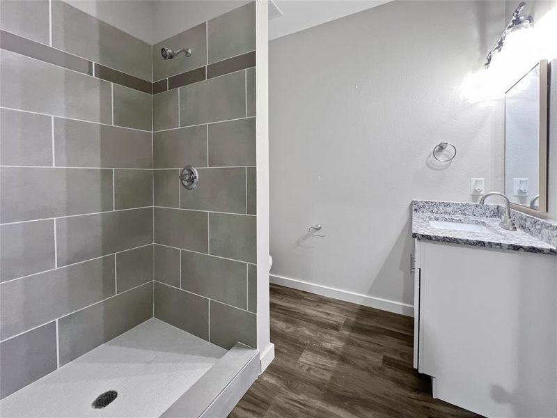 Bathroom featuring wood-type flooring, vanity, toilet, and tiled shower