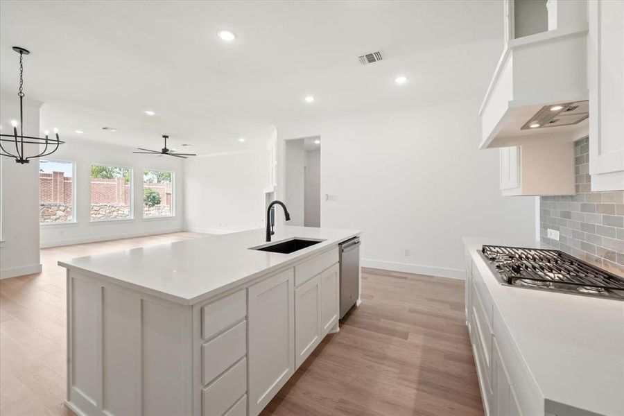 Kitchen featuring an island with sink, light hardwood / wood-style floors, hanging light fixtures, decorative backsplash, and sink