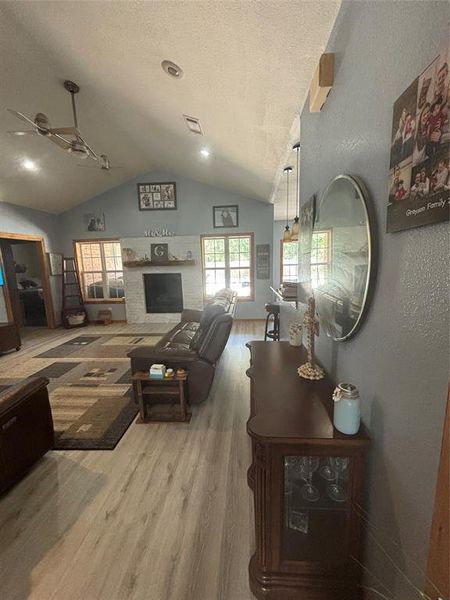 Living room with vaulted ceiling, a textured ceiling, hardwood / wood-style floors, and ceiling fan