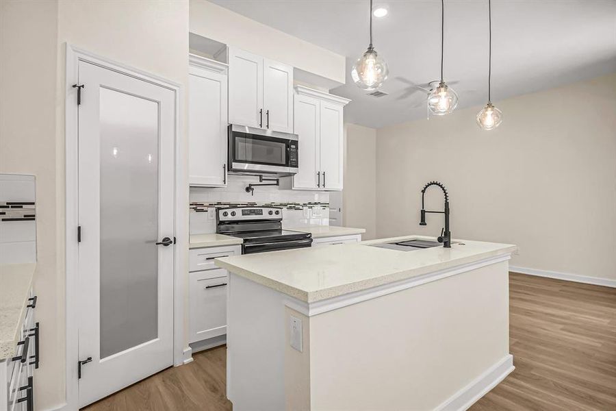 Kitchen is open to the living room beyond. Corner walk in pantry provides plenty of storage. Pot filler, designer tile backsplash and varied cabinet heights provide interest in this efficient kitchen.