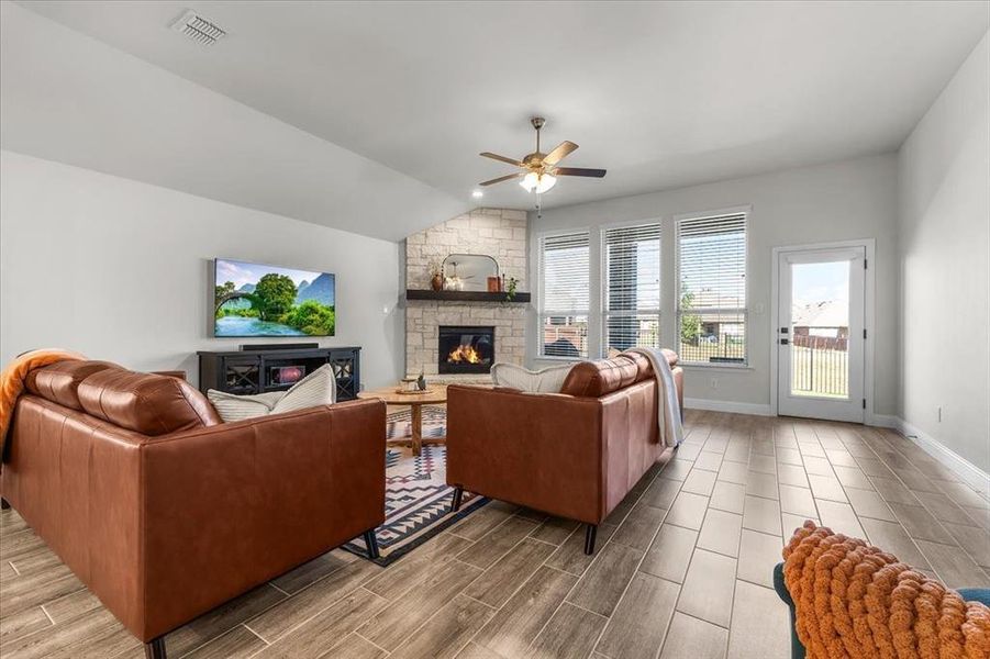 Living room with vaulted ceiling, light hardwood / wood-style flooring, a stone fireplace, and ceiling fan