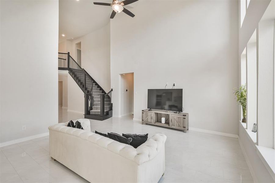 This is a spacious, modern living room with high ceilings, large windows for natural light, an elegant staircase leading to the second floor.