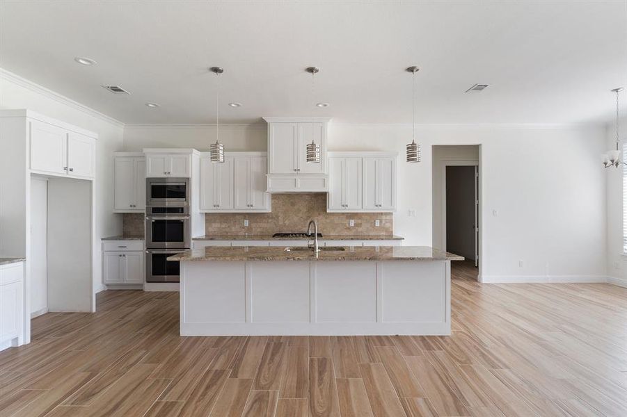 Kitchen with tasteful backsplash, pendant lighting, white cabinets, light stone countertops, and appliances with stainless steel finishes