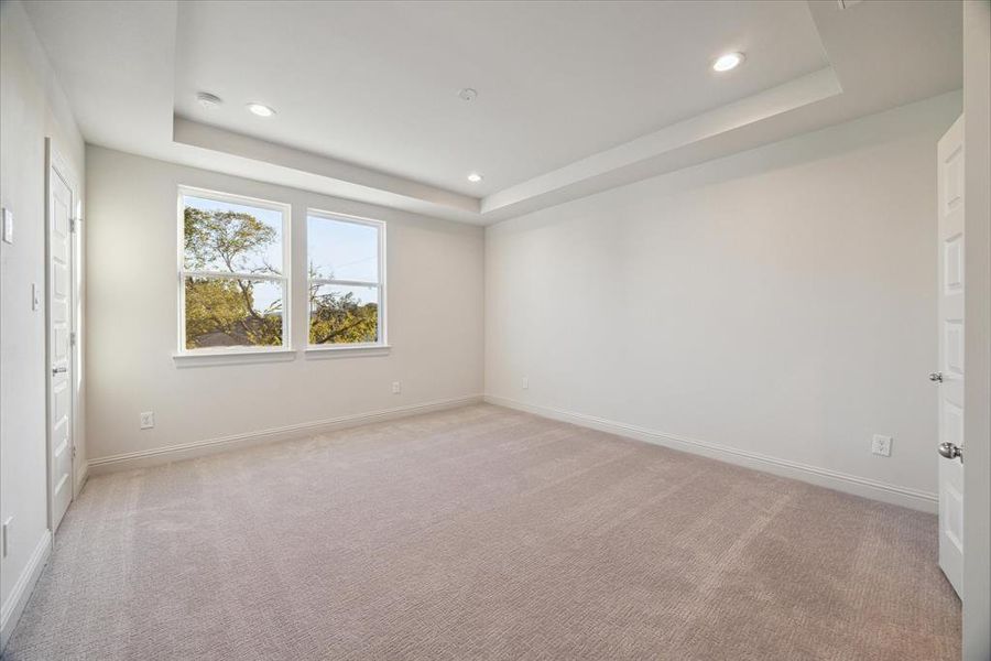 Located on the third floor, this serene primary bedroom offers a peaceful retreat with its soft neutral palette, plush carpeting, and tray ceiling detail. Large windows flood the space with natural light, creating a bright and airy ambiance. With plenty of space for furniture and design personalization, this room provides a perfect sanctuary at the end of the day.