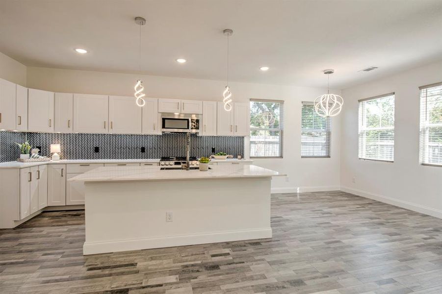 Kitchen featuring white cabinetry, light hardwood / wood-style flooring, hanging light fixtures, and a kitchen island with sink