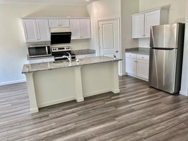 Kitchen with appliances with stainless steel finishes, a kitchen island with sink, white cabinets, and dark wood-type flooring