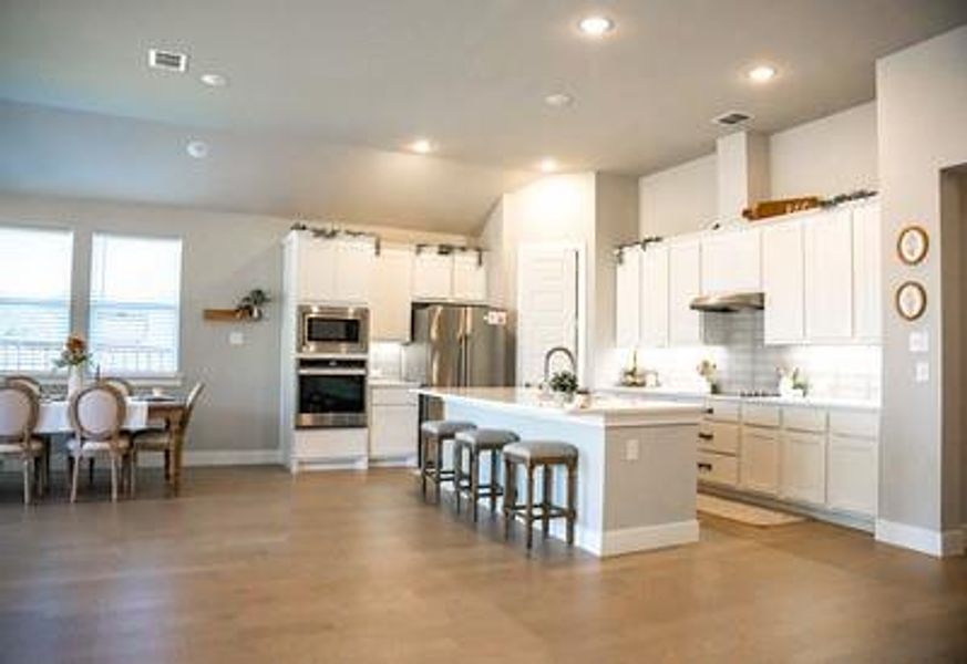 Kitchen featuring appliances with stainless steel finishes, a kitchen island with sink, hardwood / wood-style flooring, and white cabinetry