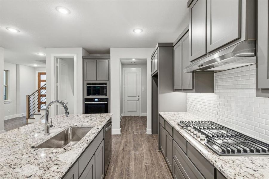 Kitchen with tasteful backsplash, sink, light stone countertops, appliances with stainless steel finishes, and dark wood-type flooring