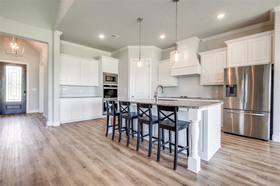Kitchen featuring premium range hood, stainless steel appliances, light wood-type flooring, backsplash, and a kitchen island with sink