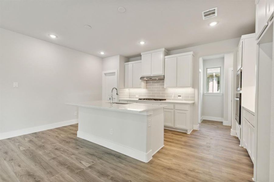 Kitchen featuring light wood-type flooring, appliances with stainless steel finishes, white cabinetry, and a kitchen island with sink