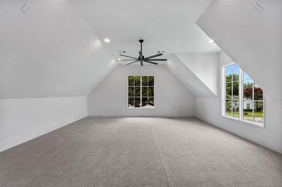Bonus room with lofted ceiling, light colored carpet, and ceiling fan