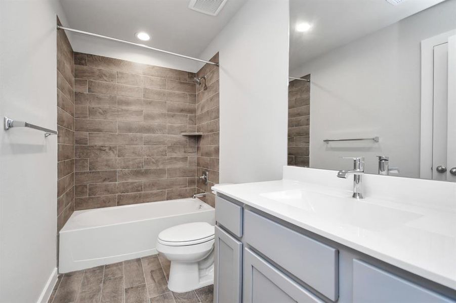 Secondary bathroom equipped with bath/shower combo surrounded by tasteful tile. Light wood cabinet paired with light countertop elevate the space.