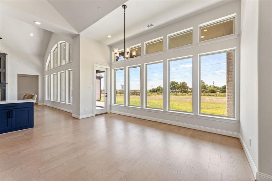 Unfurnished living room featuring light hardwood / wood-style flooring, high vaulted ceiling, and an inviting chandelier