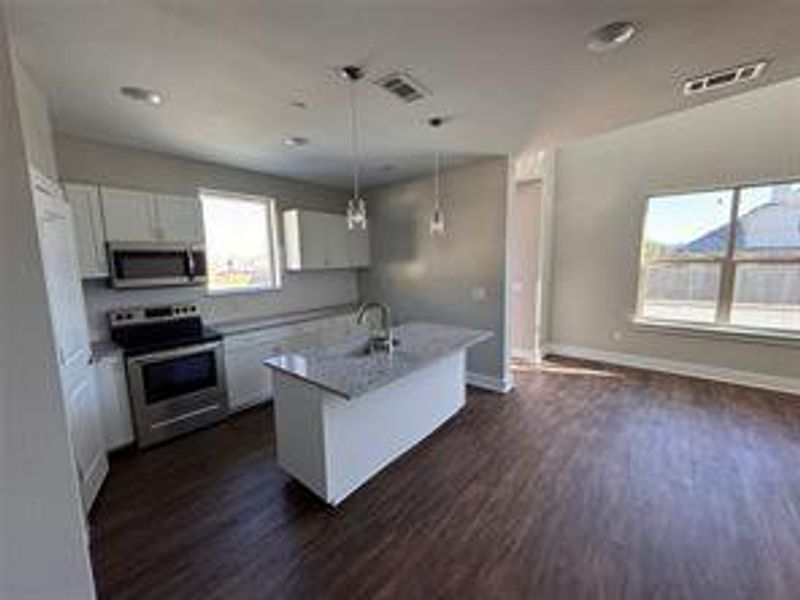 Kitchen with appliances with stainless steel finishes, an island with sink, white cabinets, decorative light fixtures, and dark hardwood / wood-style floors