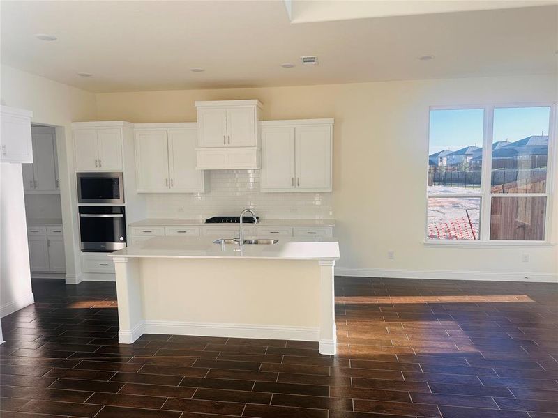 Kitchen with sink, dark wood-type flooring, an island with sink, and white cabinets