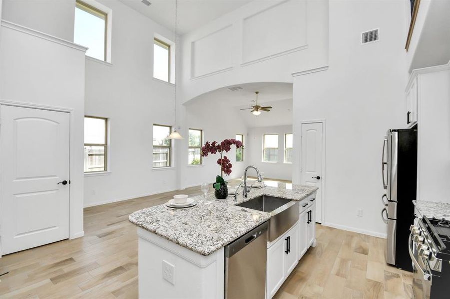 This is a bright, modern kitchen featuring high ceilings with large windows, stainless steel appliances, a central island with a sink, and light flooring.