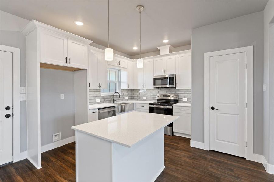 Kitchen with pendant lighting, white cabinets, dark wood-type flooring, and appliances with stainless steel finishes