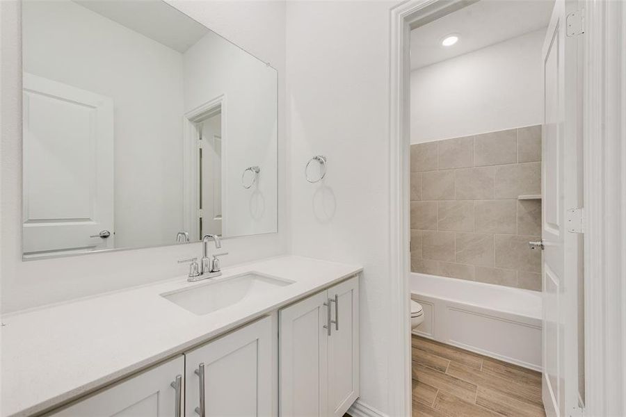 Full bathroom with wood-type flooring, vanity, tiled shower / bath combo, and toilet