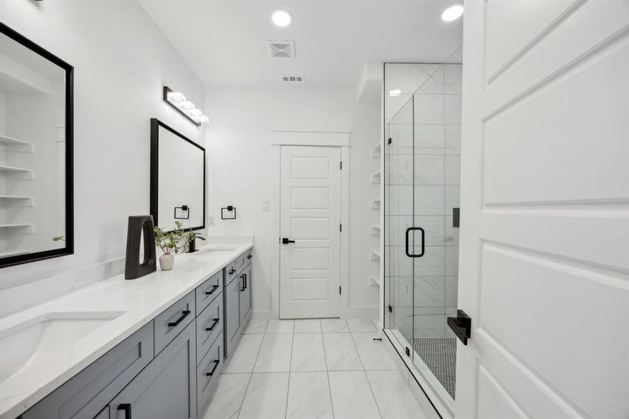 Primary with tile patterned floors, a shower with door, and double sink vanity