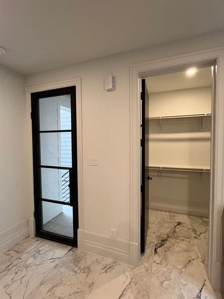 The photo shows the unit's front door, with a wooden finish and a silver handle, framed by white walls and a gray tiled entryway.