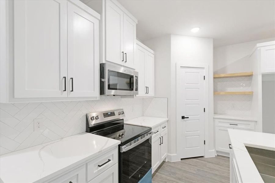 Kitchen with light hardwood / wood-style flooring, stainless steel appliances, light stone countertops, decorative backsplash, and white cabinets