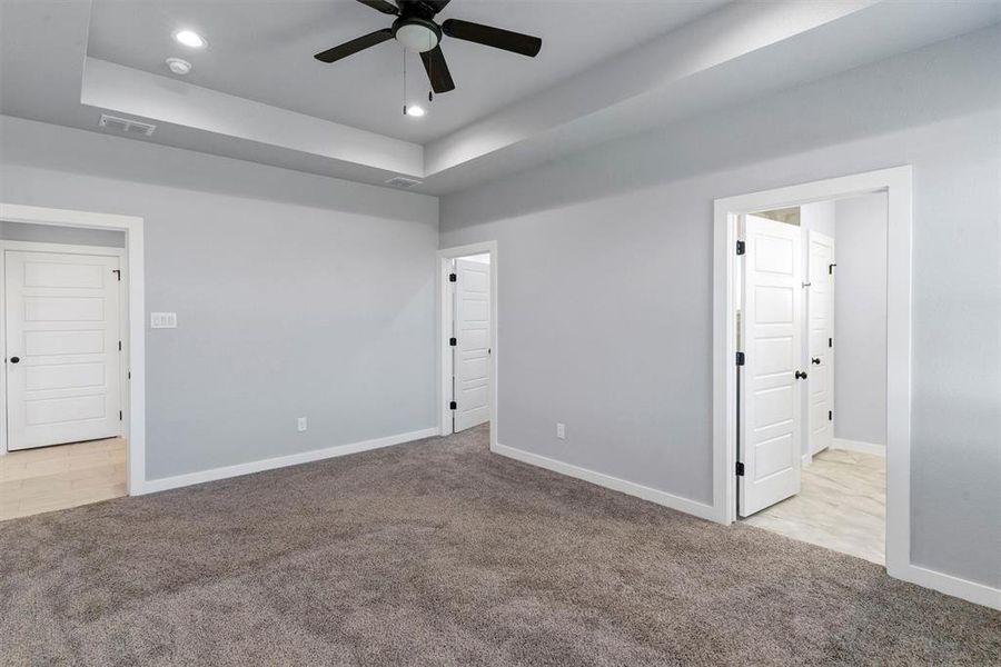 Carpeted spare room with a tray ceiling and ceiling fan