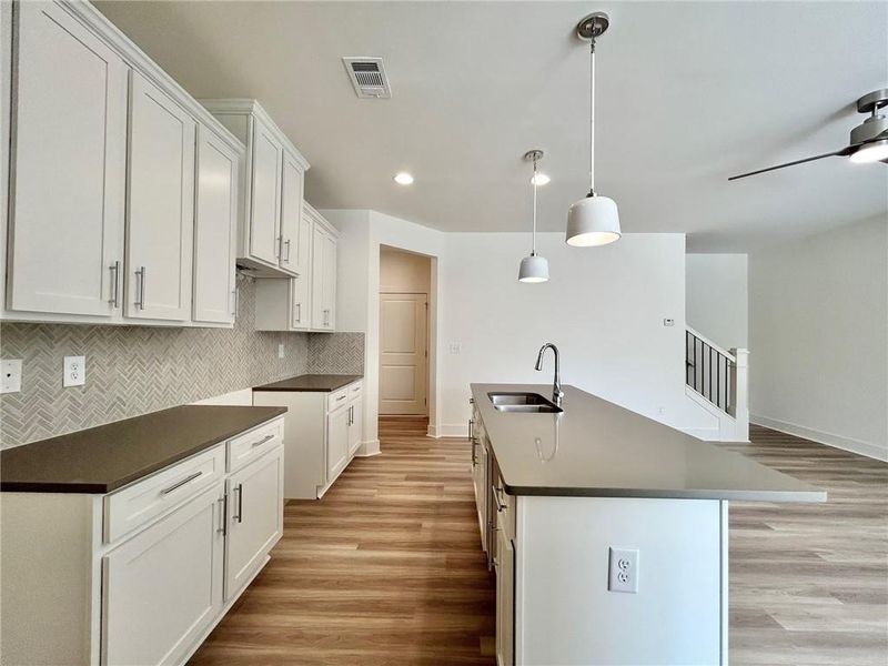 Kitchen with an island with sink, sink, light hardwood / wood-style floors, ceiling fan, and backsplash