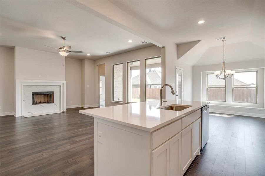 Kitchen with ceiling fan with notable chandelier, a high end fireplace, decorative light fixtures, a kitchen island with sink, and sink