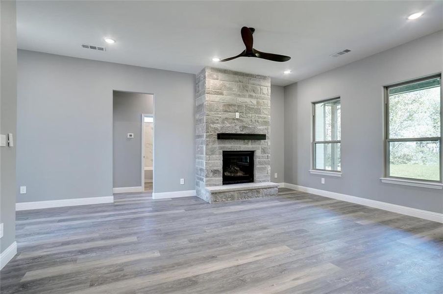 Unfurnished living room featuring wood-type flooring, plenty of natural light, ceiling fan, and a fireplace